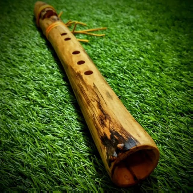 A pale hand-carved branch flute lying on green grass