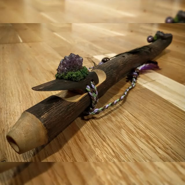 A dark wood flute with an amethyst crystal block and woven cord