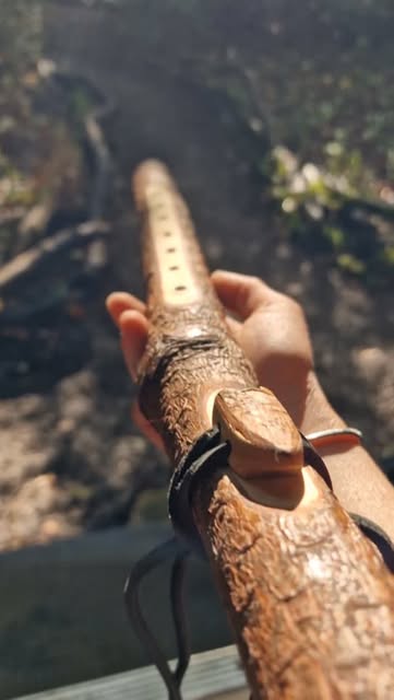 A hand holding a bark-covered flute with a carved bird block