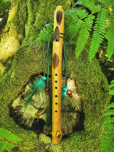 A Woodland flute with turquoise feathers and beads resting on moss among ferns